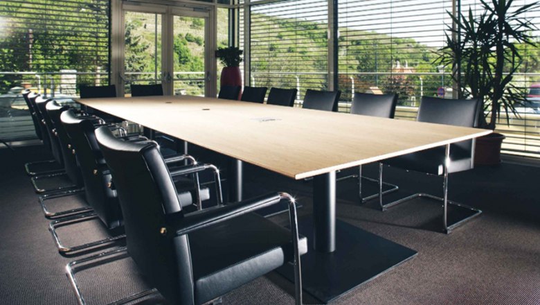 Steigenberger Krems, seminar room Spitz, © Steigenberger Hotel and Spa, Andreas Hofer Modern seminar room with large wooden table and black chairs, surrounded by glass walls with a view of the green landscape.