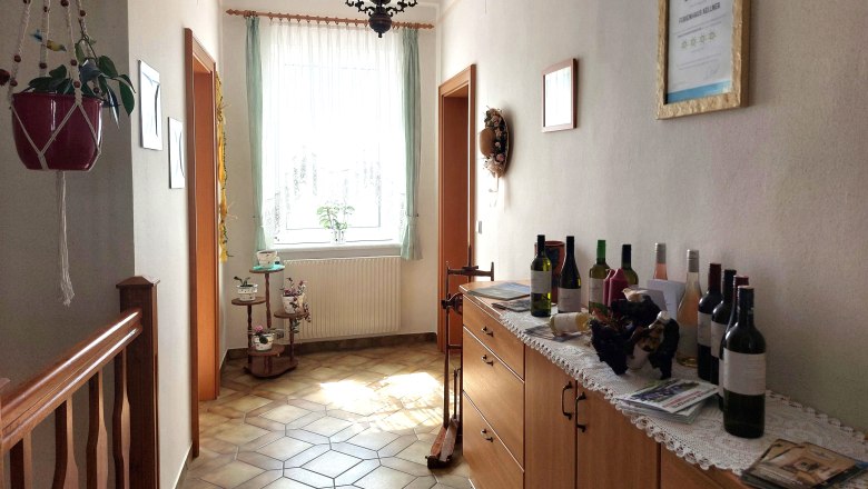 Anteroom, © Erika Kellner A bright anteroom with tiled floor, a chest of drawers with wine bottles and a window with curtains.