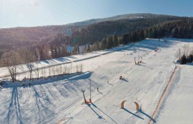 Family ski area at the Wexl Arena St. Corona am Wechsel, © Wexl Arena St. Corona am Wechsel Aerial view of a snow-covered ski resort with slopes and forest in the background.