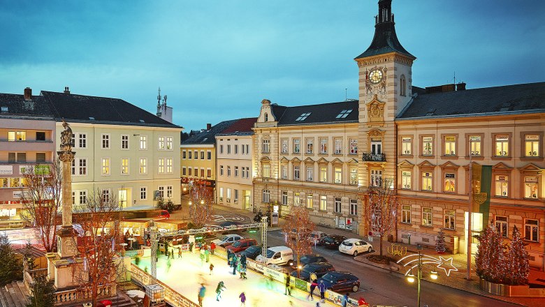 Advent magic at the ice rink, © Alexander Bernold Ice rink in a town at dusk, surrounded by historic buildings and Christmas lights.