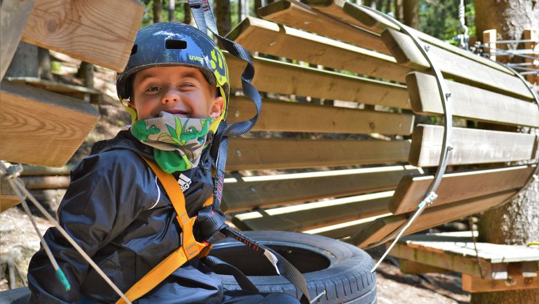 Children's course, © Hamari Kletterpark A child wearing a helmet and safety harness in a climbing park.