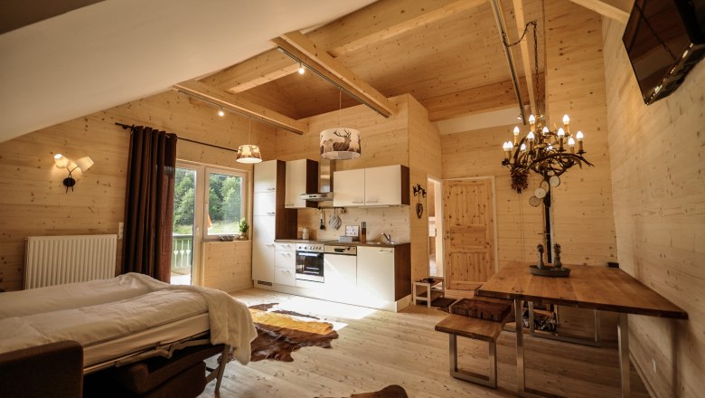 Styrian Apartment, © Stefan Zimprich Cozy apartment with wooden walls, kitchen, dining table and bed.