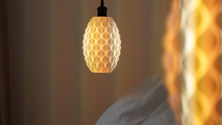 Country house Krell, © Weingut Krell Close-up of a hanging lamp with a honeycomb pattern emitting warm light next to a bed.