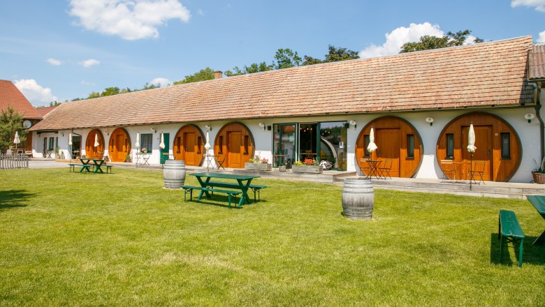 Winery Küssler, © Winzerhof Küssler A long building with round wooden doors and a well-tended lawn in front of it with picnic tables and wine barrels.
