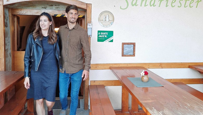 Buschenschank (typical tavern) Gratzer-Sandriester, Prellenkirchen, © Donau Niederösterreich, Neubauer A man and a woman leave a Buschenschank (typical tavern) called Gratzer-Sandriester. They smile and walk past wooden benches.