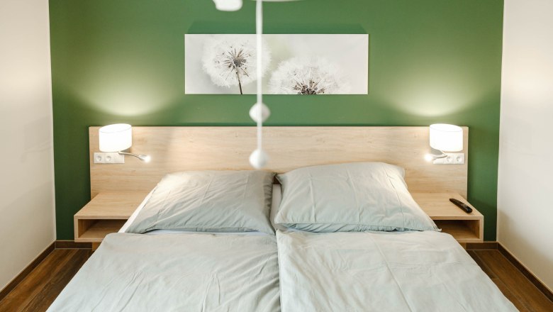 Bedroom Grüne Veltliner, © Michael Reidinger Modern bedroom with green-painted wall, double bed and two bedside lamps.