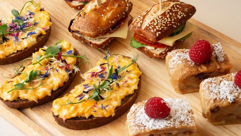 Fine coffee breaks at a seminar, © Sporthoel Semmering Various snacks on a wooden board, including sandwiches, sandwiches and pastries with raspberries.