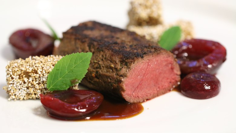 Delicacies from the award-winning kitchen, © Familie Görg Gourmet dish with pink roasted meat, fruit and herbs served on a white plate.