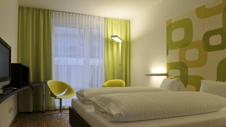arte Hotel, © arte Hotel Modern hotel room with double bed, green-yellow curtains and wall decor.