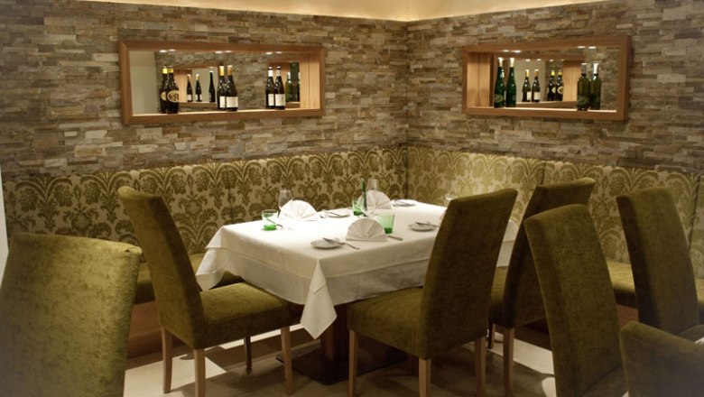 Restaurant Gartenhotel Pfeffel, © Alexander Pfeffel Elegant restaurant with laid table and green chairs.