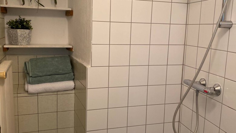 Shower, © Familie Stagard A tiled shower with shower head, towels and plants on shelves.