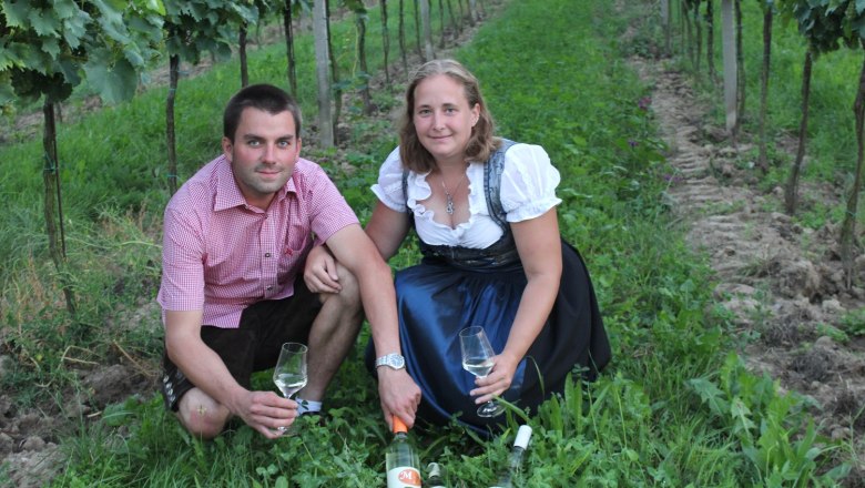 Viticulture Fitz, © Weinbau Fitz Two people are sitting in a vineyard with wine glasses and bottles.