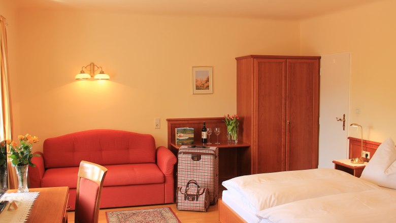 Double room Superior, © Schendl A cozy hotel room with a double bed, red sofa, wooden furniture and flowers.