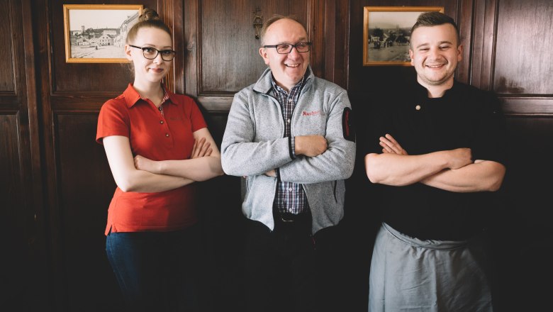 Pub team, © Niederösterreich Werbung/Mara Hohla Three people stand smiling with their arms folded in front of a wooden wall.