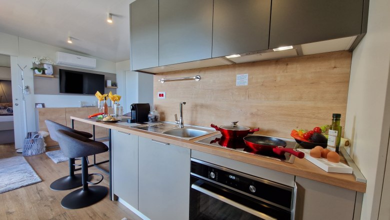 Kitchen of the Johannesbachklamm Chalet, © Johannesbachklamm Chalet Modern kitchen with gray cabinets, stove, sink and bar stools.