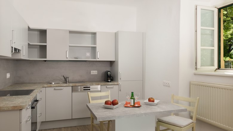 Kitchen, © Landhaus Puchbergerhof by smc Modern kitchen with gray cabinets, table with apples and drink, open window.