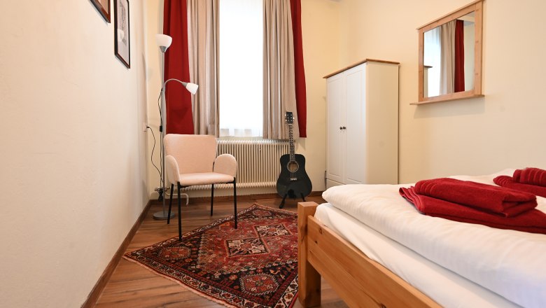 Small room, © Christine Kuppelwieser Small room with bed, carpet, chair, floor lamp, guitar and wardrobe.