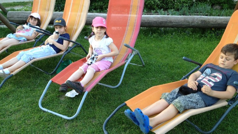 Kerndlerhof deckchairs for children, © Kerndlerhof Four children are lying on deckchairs in the garden holding small animals.