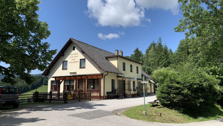 Polleres Inn, © TVB Semmering-Rax-Schneeberg A yellow inn with the inscription 'Polleres Gasthof zum Kreuzberg' surrounded by trees and a blue sky.