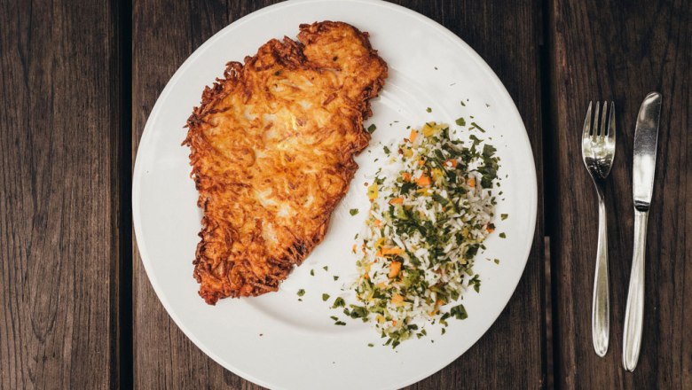 Potato breaded schnitzel, © Niederösterreich Werbung/Daniela Führer A plate with a potato cutlet and rice vegetables on a wooden table.
