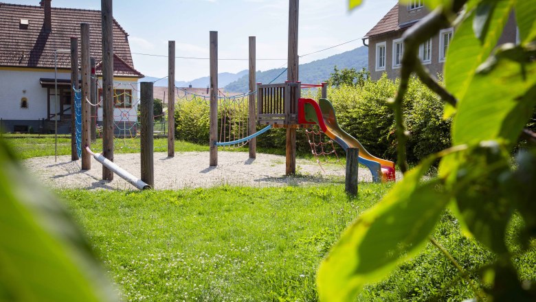 Adventure playground in Joching, © Donau NÖ Tourismus_Barbara Elser An adventure playground with climbing frame and slide, surrounded by green meadows and trees, with houses and hills in the background.