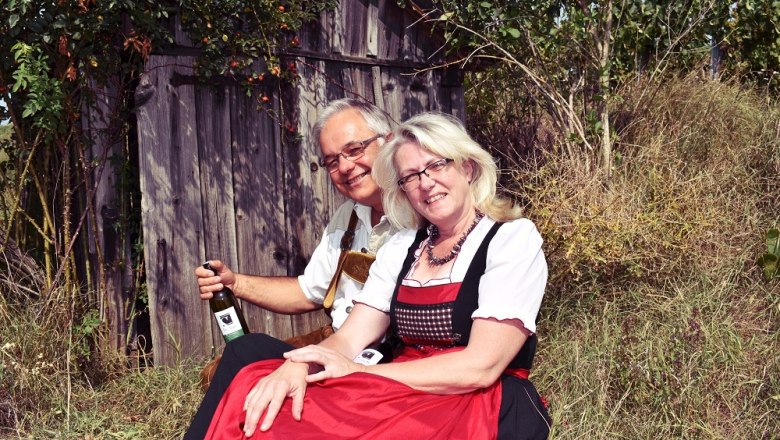 Vineyard hut, © Weingut Schober A couple in traditional dress sits in front of a wooden hut outside.