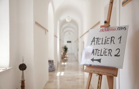 Studio, © akademie.Geras2011 A bright hallway with a sign on an easel pointing to Atelier 1 and Atelier 2.