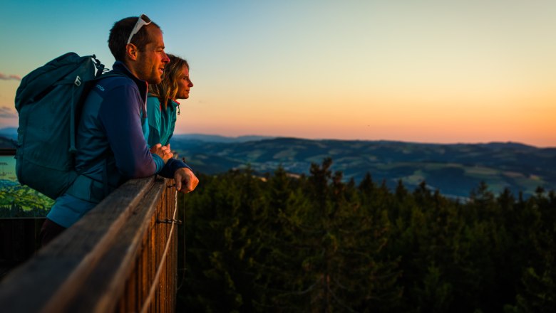 Sunrise on the viewing platform at Hutwisch, © Wiener Alpen/Martin Fülöp Two people stand on a vantage point and gaze into the distance at sunset.