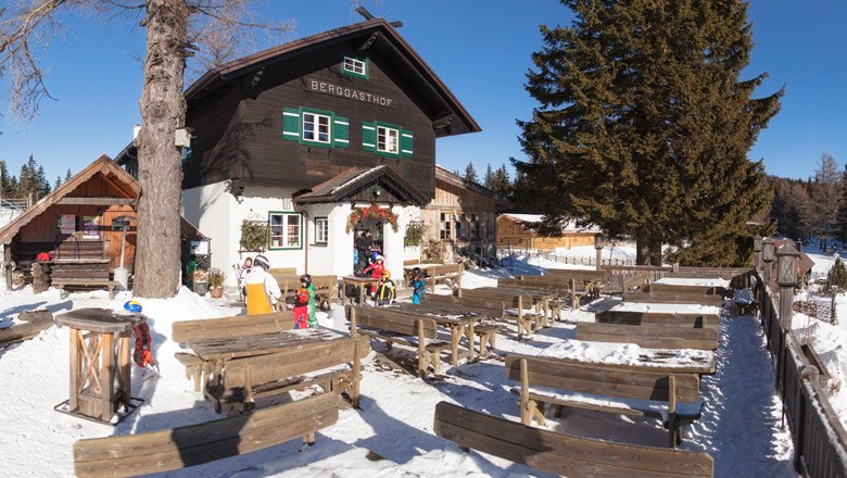 Rest at the Mönichkirchner Schwaig mountain inn, © Wiener Alpen/ Franz Zwickl Mountain inn in the snow with wooden benches and tables outside.