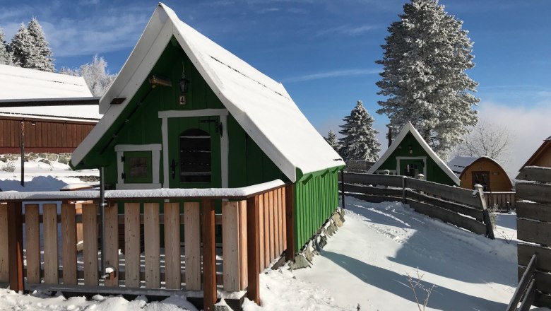 Wood Lodge, © Ernst Prutti Snow-covered wooden huts in a wintry landscape with a blue sky.