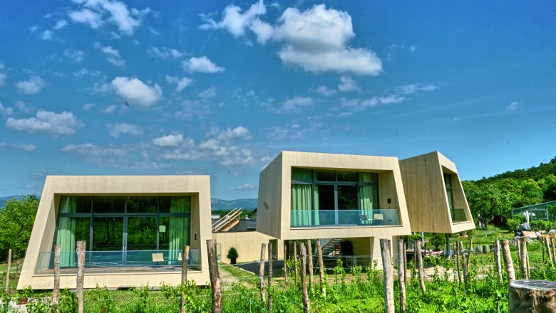 Garden lofts from Guntrams Estate, © Stefan M. Gergely Modern garden lofts with large windows and wood paneling in a green landscape under a blue sky.