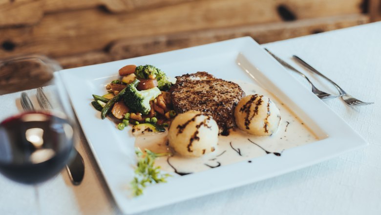 Riesling cutlet, © Niederösterreich Werbung/David Schreiber A plate with a chop, vegetables and dumplings, garnished with sauce and balsamic vinegar, on a white table.