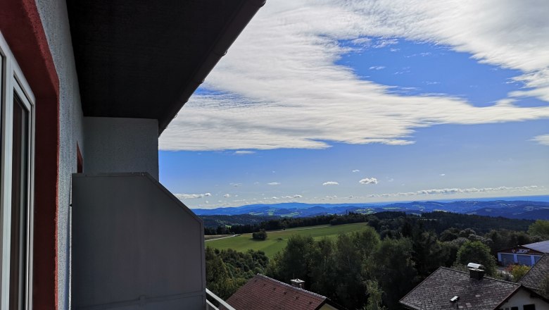 Balcony with a view, © Franz Thier View from a balcony of a landscape with houses, trees and hills under a blue sky with clouds.