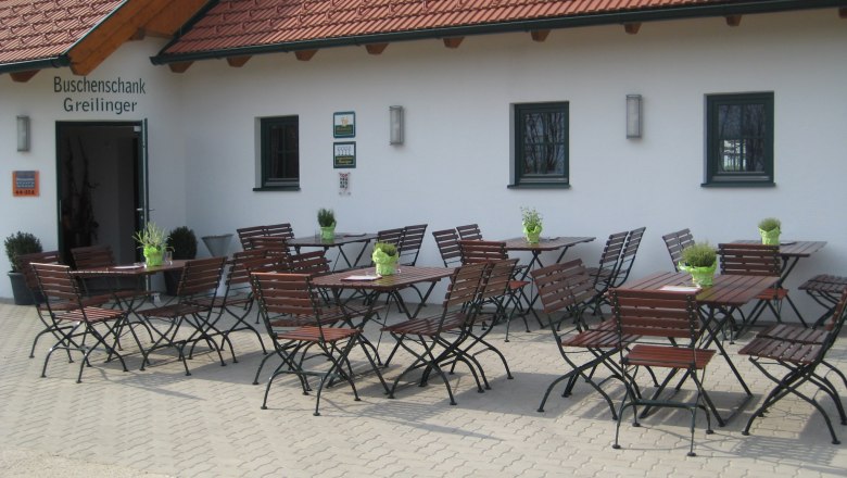 Winery & Buschenschank (typical tavern) Greilinger, © Greilinger Outdoor area of a Buschenschank (typical tavern) with empty wooden tables and chairs in front of a building with a red tiled roof.