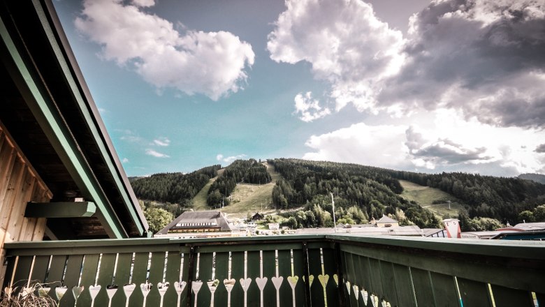 Styrian Apartment, © Stefan Zimprich View from a balcony of a green mountain landscape with clouds in the sky.