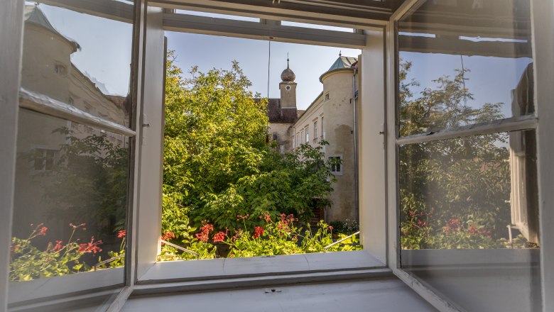 Oberstockstall Estate, © Niederösterreich Werbung / Maximilian Pawlikowsky View from an open window of a green garden and a historic building with a tower.