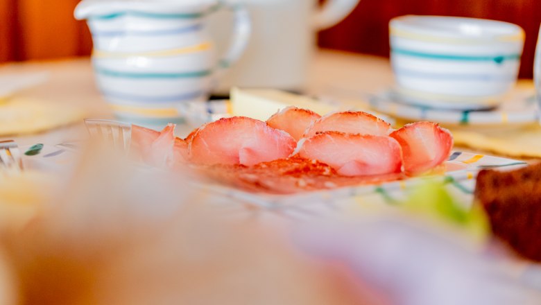 Woltron Manor, © Wiener Alpen / Christian Kremsl Close-up of a breakfast table with ham, crockery and cups.