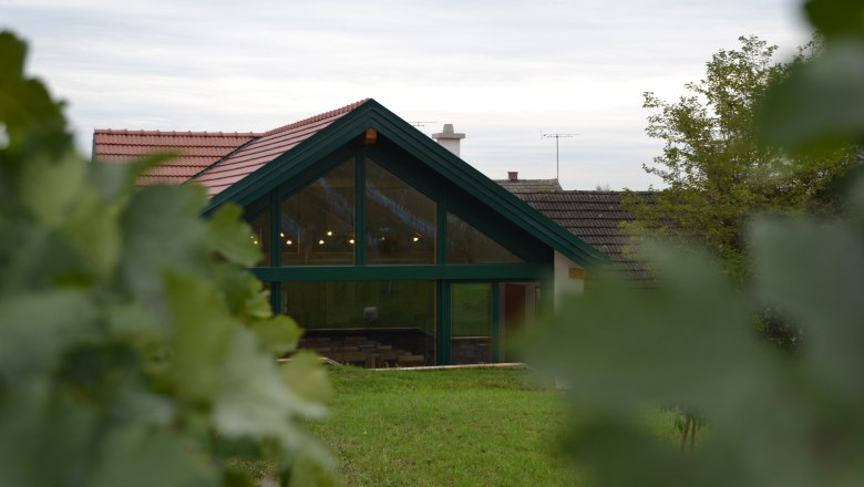 Viticulture Müllner, © Michael Müllner Modern building with glass front and red roof, surrounded by green vegetation.