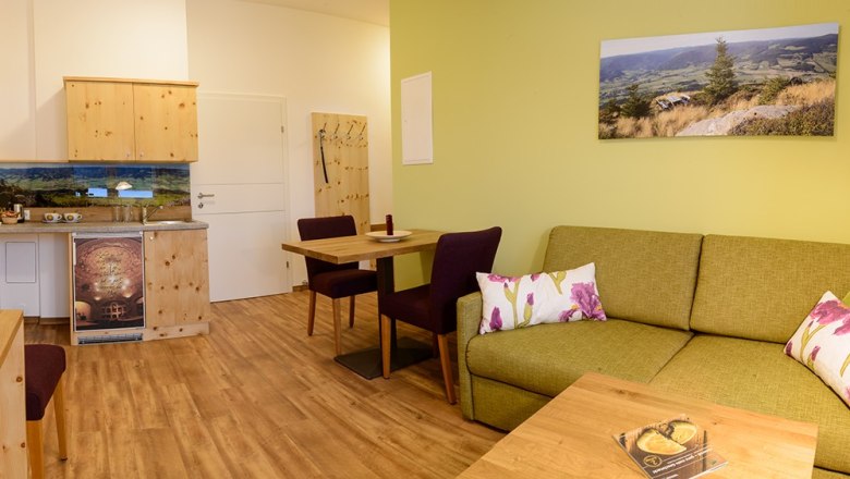 Peilstein room, © Wirtshausbrennerei Krenn, Johann Frank Cozy room with green couch, wooden furniture and landscape photo on the wall.