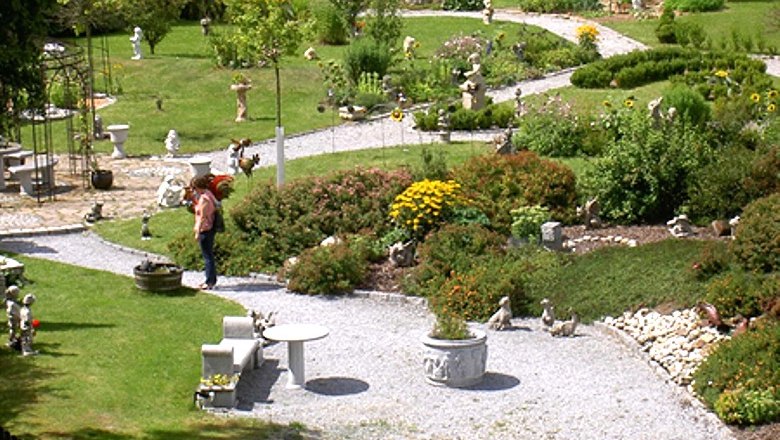 Kurt Zlabinger show garden, © Kurt Zlabinger A well-tended show garden with curved paths, flowerbeds and garden figures. A person looks at the plants.