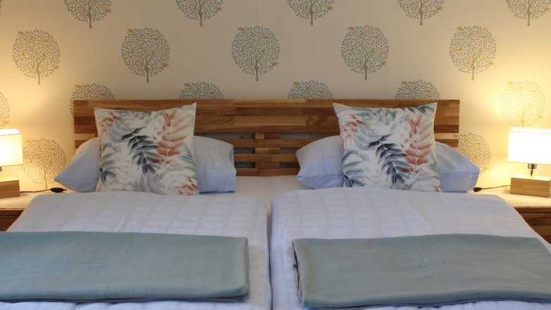 Cozy rooms, © Magdalena Donhauser Comfortable double bed with wooden headboard, blankets and pillows and bedside tables with lamps.