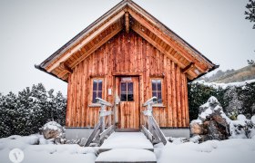 Clammy sauna, © TheVerve-Agentur (theverve.at) A small wooden hut in the snow with a steep roof and two windows.