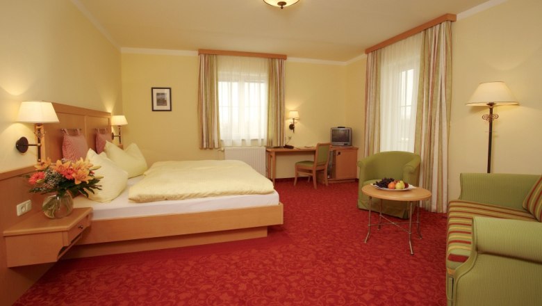 Double room, © Hotel Wachau A cozy hotel room with a double bed, sofa, table and TV. Yellow walls and red carpets dominate the room.