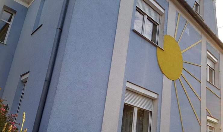House view, © Harald Mader Blue house with yellow sun decoration on the façade.