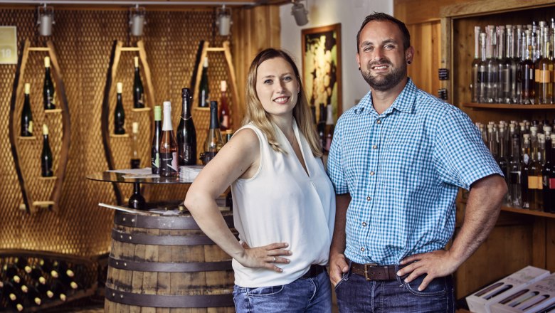 Muthenthaler farm store, © Florian Schulte Two people are standing in a farm store with bottles of wine in the background.
