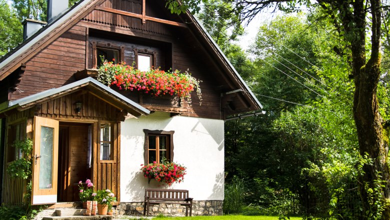 Vacation cottage Brandl, © Raffaela Huber A picturesque vacation home with wooden paneling and flower boxes, surrounded by lush greenery.