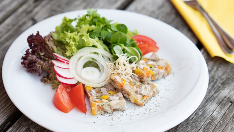 Steinerhofsulz with seed oil and horseradish, © Niederösterreich Werbung/Nadja Büchler A plate of sausage, lettuce, tomatoes, radishes and onions on a wooden table.