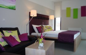 Premium bon-vivant rooms Zur Schonenburg, © Gasthof Hotel "Zur Schonenburg" Modernly furnished hotel room with double bed, sofa and decoration in shades of purple and green.