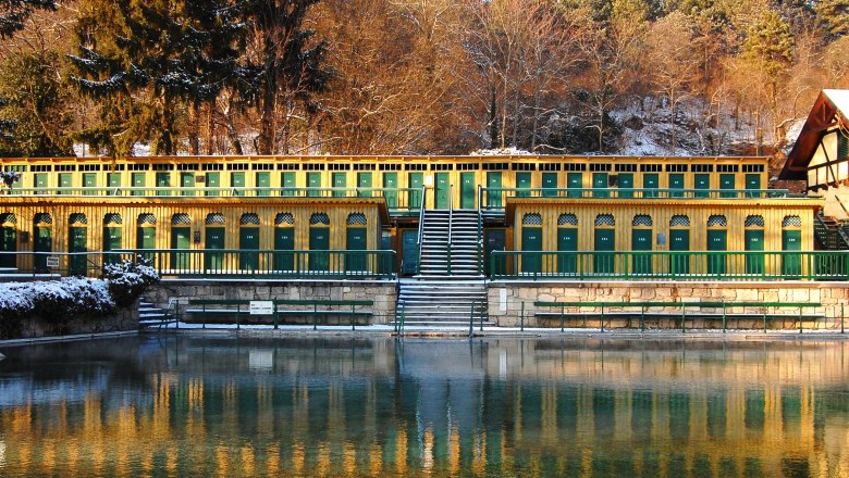 Fischau thermal baths - after the sauna in the refreshing thermal water, © Marktgemeinde Bad Fischau-Brunn Historic thermal bath with yellow and green cabins, surrounded by trees in winter.