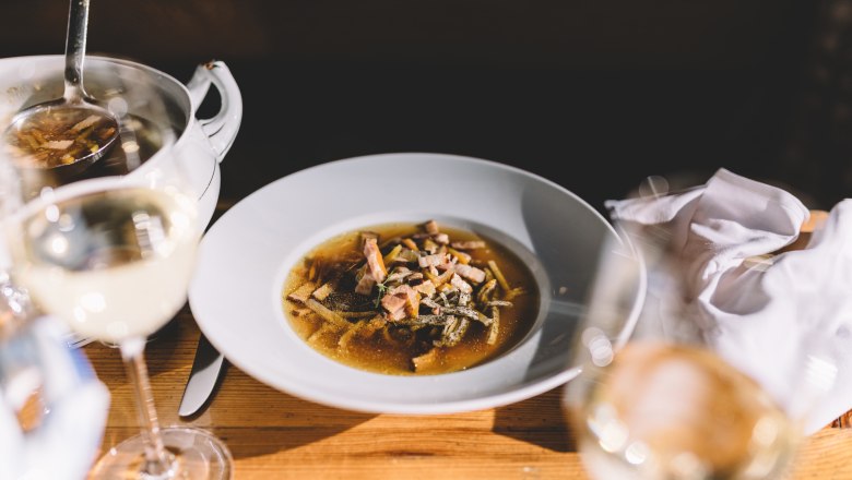 Rye beer soup with poppy seed pancakes, © Niederösterreich Werbung/Mara Hohla A plate of rye beer soup and poppy seed pancakes on a wooden table, with a glass of white wine next to it.